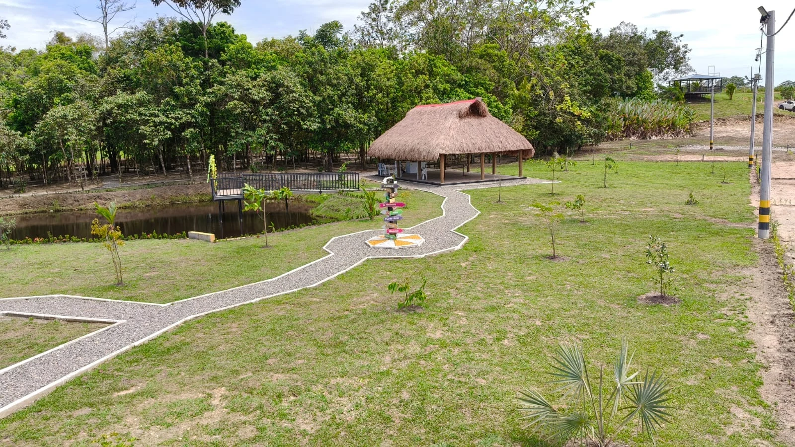 Lago, kiosco con techo de palma y senderos entre árboles en Verdecielo