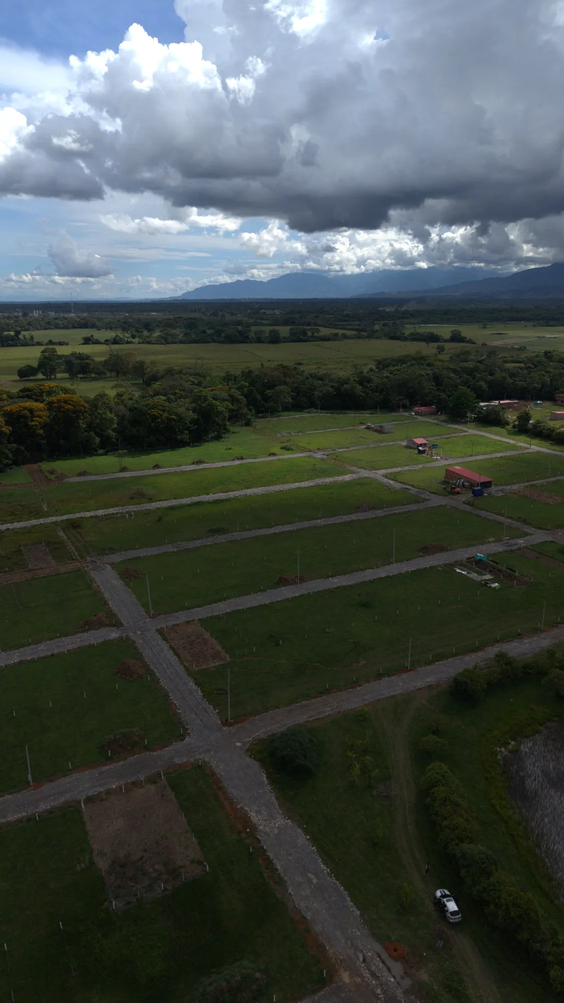 Lotes demarcados con postes blancos entre vías abiertas, bosque y montañas al fondo
