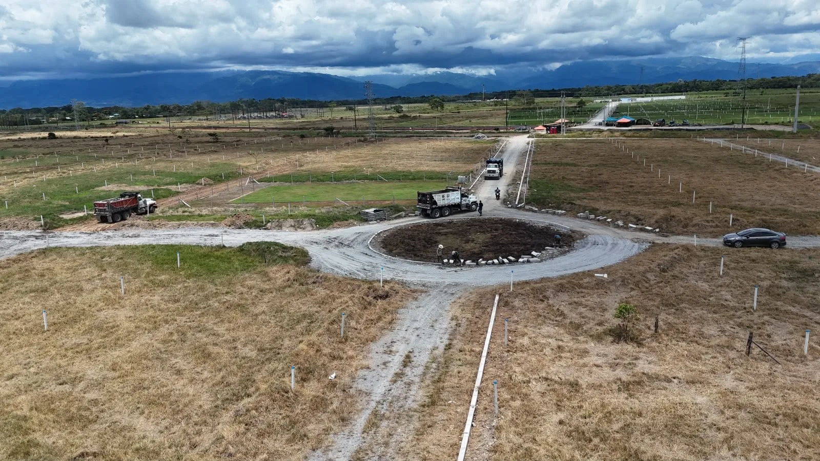 Glorieta en construcción con lotes demarcados y montañas al fondo