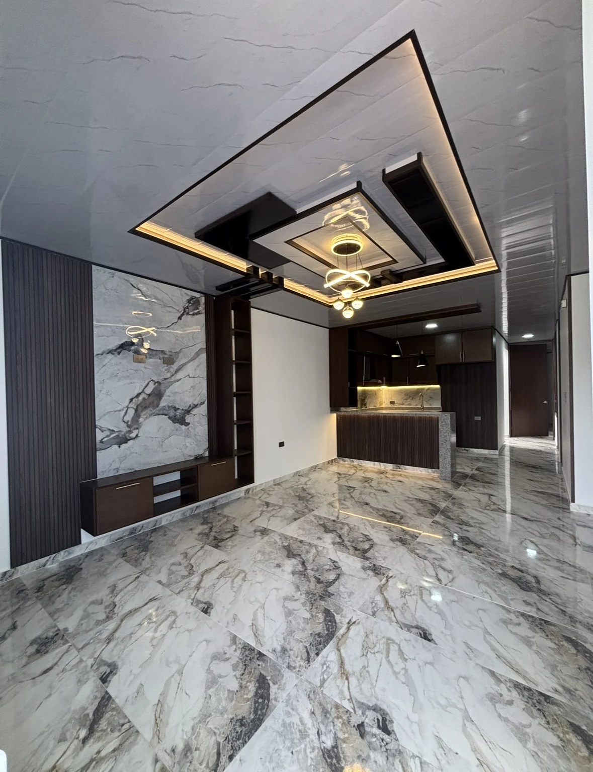 Interior de casa en venta: sala con mueble de tv en madera y mármol, cocina integral y techo con iluminación indirecta